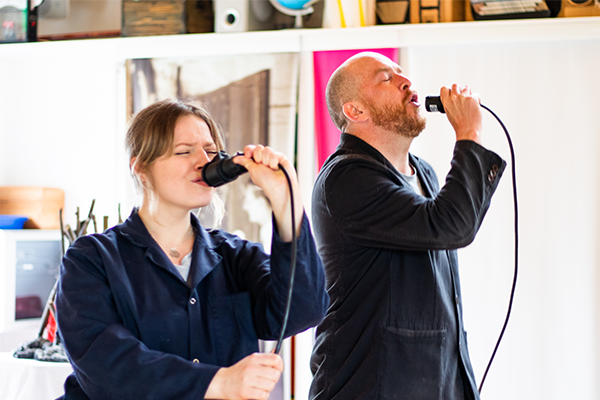 Ed and Emily sing comically into pretend microphones made from 16amp electric cables.